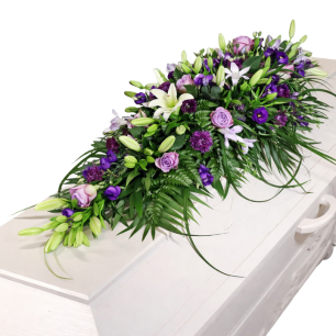 Vit kista dekorerad med ett blomsterarrangemang av lila och vita blommor samt gröna blad.