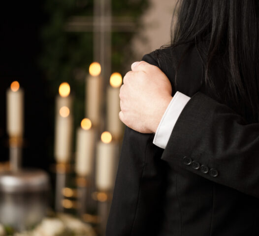 En person i svart kostym håller om en annan person framför tända ljus.