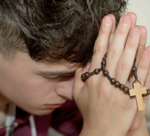 En person med huvudet lutat mot händerna som håller ett radband med ett kors.